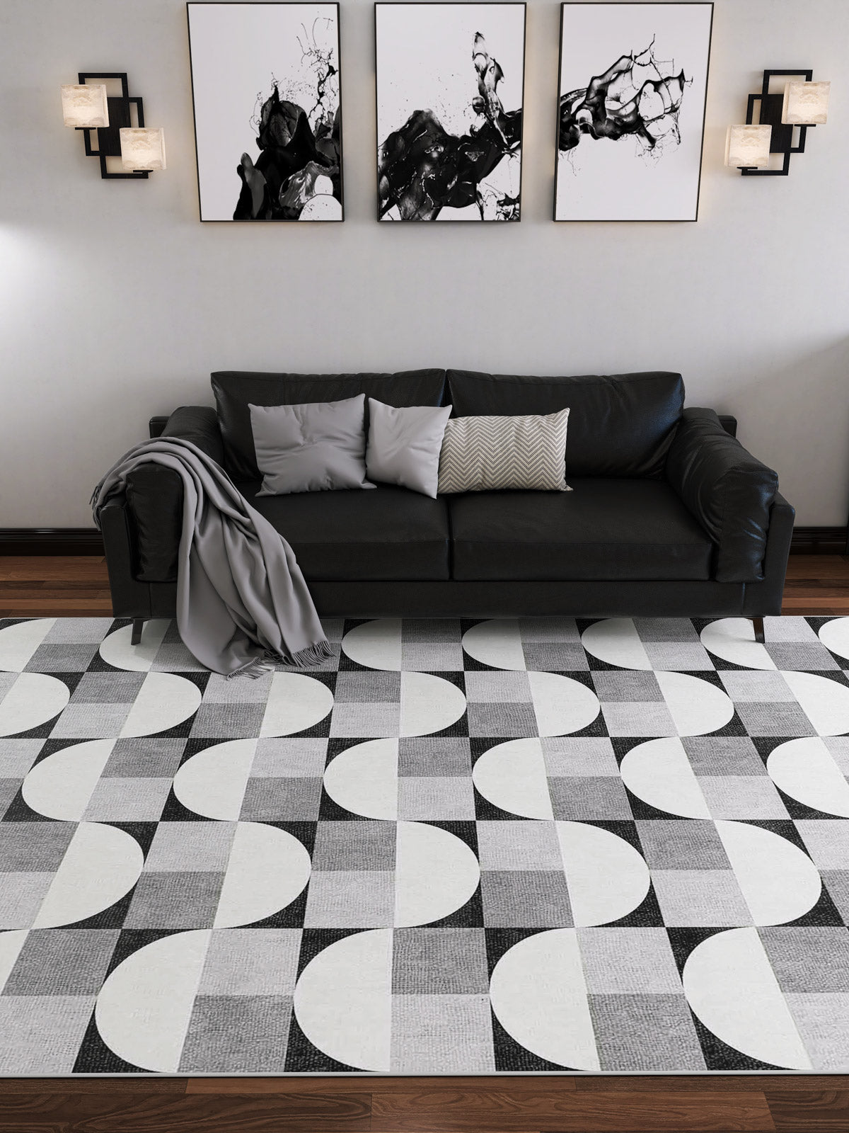 A modern living room with a black leather sofa, three cushions, a gray throw, abstract black-and-white art, wall sconces, and the Patina Bloom - Washable Rug - JRN50 (Custom Size)—a chic addition to stylish modern interiors.
