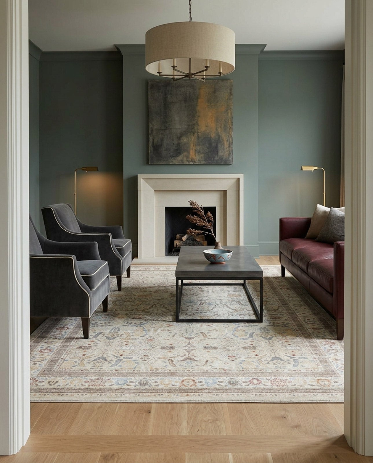 A modern living room with green walls, a large abstract painting over a white fireplace, two dark armchairs, a brown leather sofa, a rectangular coffee table, and the Pearl Oushak - Area Rug - APX2931 on wood flooring.