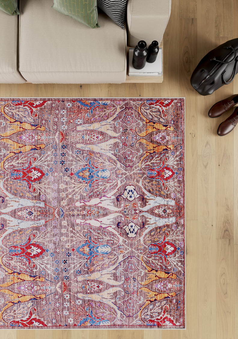 The Peregrine Peachy Brown Washable Rug - LCC3022 (Custom Size) sits on a light wooden floor near a beige sofa, stacked books, and brown shoes—ideal for high-traffic areas and easy to clean.