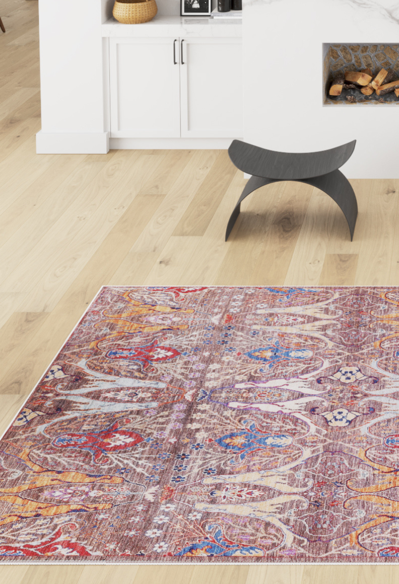 The Peregrine Peachy Brown Washable Rug - LCC3022 (Custom Size) adds color and pattern to a modern living room with white cabinetry, a fireplace, woven basket, and black curved stool—great for high-traffic spaces.