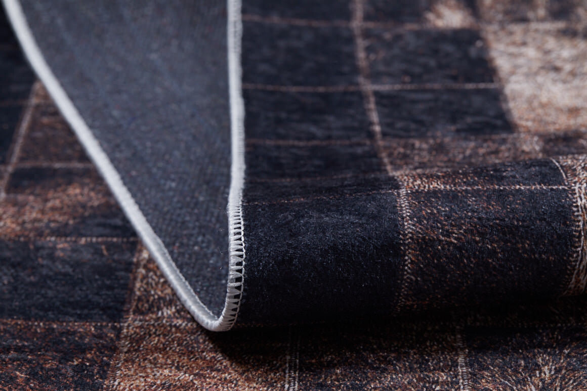 A close-up of the Pinstripe Paradise - Washable Rug - JR1004 (Custom Size) shows its dark brown and black bronze pattern, white stitched edge, textured surface, and underside as the washable rug is partially folded.