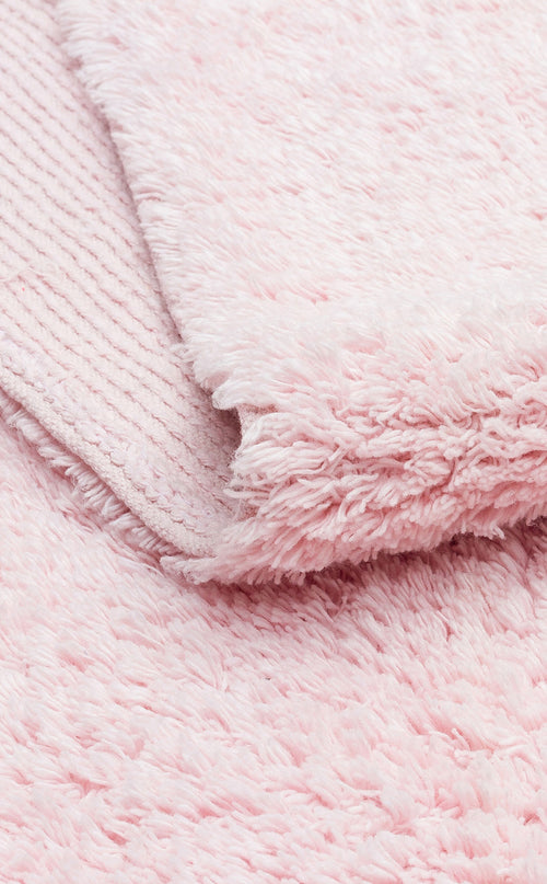 Load image 1 in gallery view. A close-up of Powder Calm - Washable Shaggy - CBNPLAIN shows its soft, fluffy light pink texture, with one edge folded to reveal a ribbed underside contrasting the plush surface.
