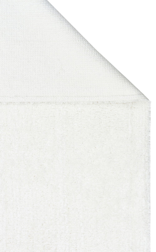 Load image 1 in gallery view. A close-up of the Pure Thread - Washable Shaggy - CBNPLAIN white cotton rug, with one corner folded over to highlight its textured front and smoother back.