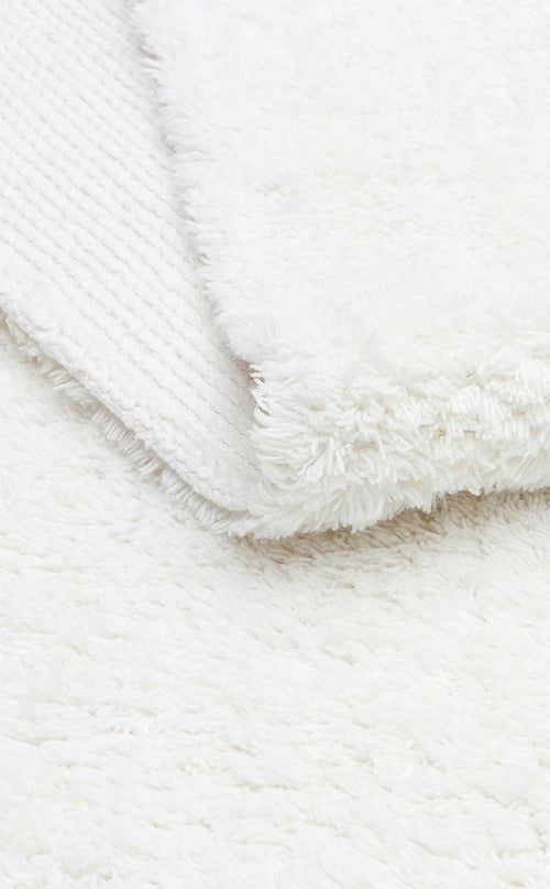 Load image 1 in gallery view. Close-up of the Pure Thread - Washable Shaggy - CBNPLAIN rug in white, with a corner flipped to show its textured underside. This cozy, plush rug features a soft, shaggy surface and is fully washable for easy care.