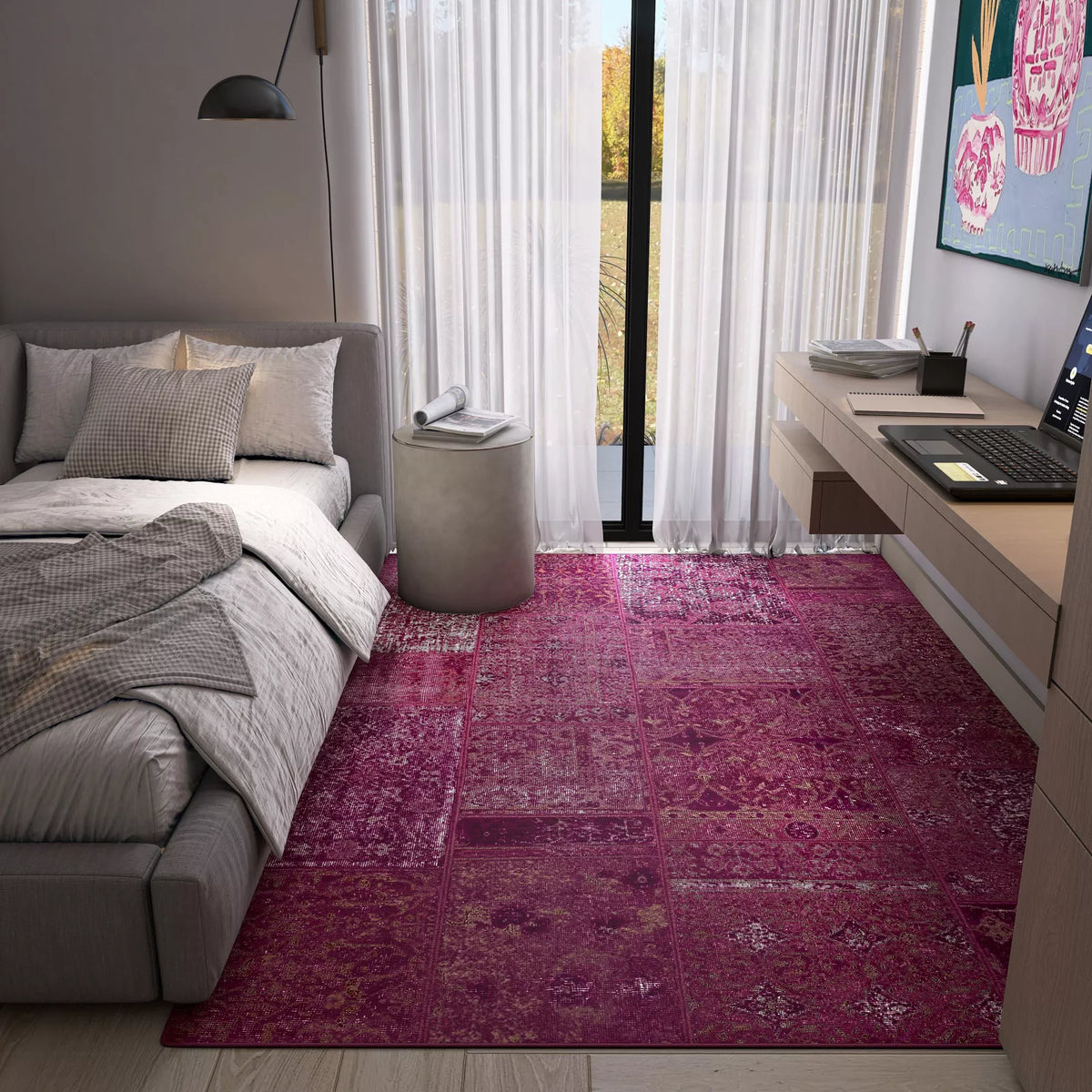 A cozy modern bedroom with a gray bed, round side table, built-in desk, and the Purple Mist - Washable Rug - JRN1038 in vibrant pink—ideal for high-traffic areas. Sheer curtains let natural light fill the room.
