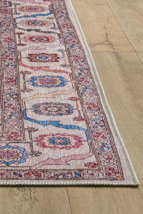 Load image 1 in gallery view. A close-up of the Quasar Traditional Washable Rug - LCC3024 shows its detailed pink, blue, and beige pattern, textured edge, and intricate border on a light wooden floor.