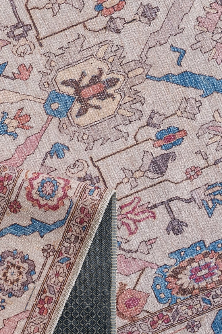 A close-up of the Quasar Traditional Washable Rug - LCC3024 showcases its blue, pink, cream, and beige geometric and floral flat weave. A folded corner reveals the washable rug’s woven mesh backing underneath.