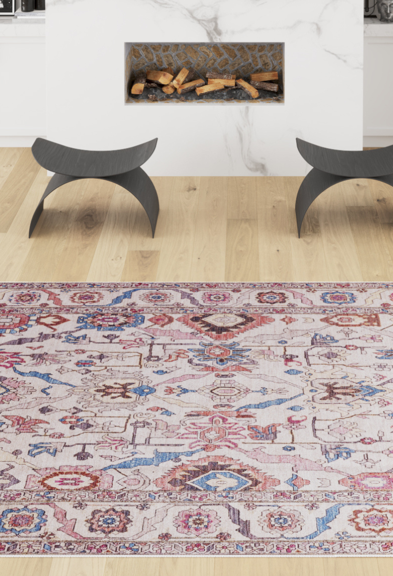 The Quasar Traditional Washable Rug - LCC3024 (Custom Size), featuring red, blue, cream, and beige patterns, sits on a light wood floor by a modern white marble fireplace with two black curved stools—ideal for high-traffic areas.