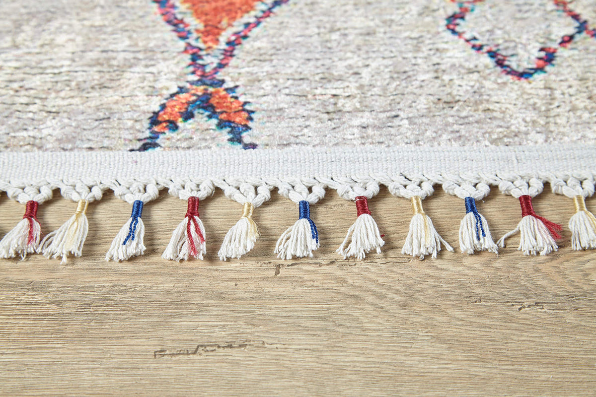 Close-up of the Rainbow Rhapsody - Washable Rug - JR5060 (Custom Size) edge, featuring knotted white fringe with some tassels in blue or red, on a light wood floor. Its colorful geometric pattern is ideal for high-traffic areas.