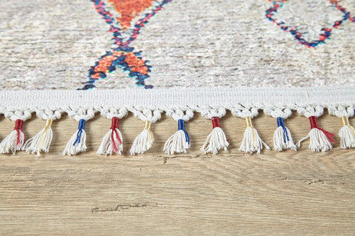 Load image 1 in gallery view. Close-up of the Rainbow Rhapsody - Washable Rug - JR5060 (Custom Size) edge, featuring knotted white fringe with some tassels in blue or red, on a light wood floor. Its colorful geometric pattern is ideal for high-traffic areas.