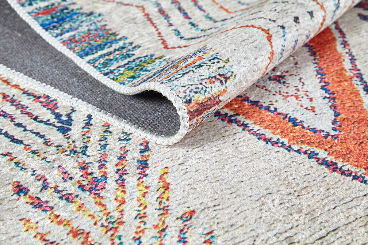 A close-up of the Rainbow Rhapsody - Washable Rug - JR5060 (Custom Size) shows its vibrant orange, blue, and yellow geometric and abstract patterns on a light background. The textured, washable surface is perfect for high-traffic areas.