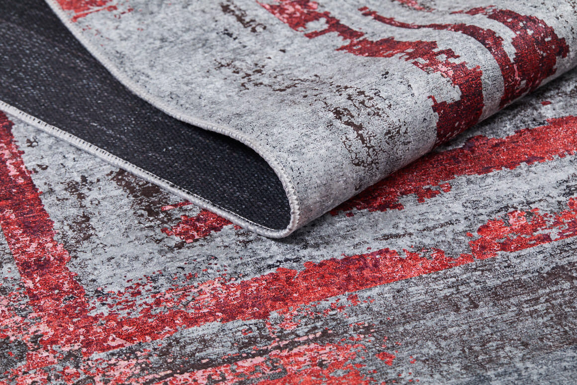 A close-up of the Refined and Timeless - Washable Rug - JR1500 (Custom Size) shows its gray and red abstract distressed pattern, black underside, and folded corner—ideal for high-traffic areas.