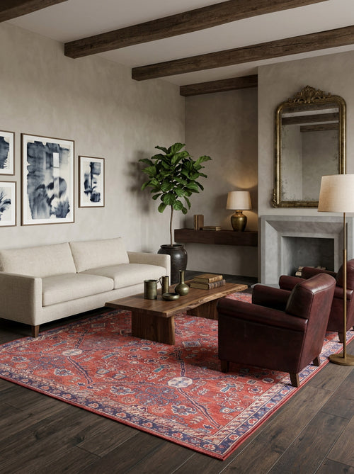 Load image 1 in gallery view. A cozy living room with a beige sofa, a Rhapsody Authentic Red Washable Rug - LCC3033, a wooden coffee table, a dark leather armchair, abstract art, a tall plant, floor lamp, and fireplace topped with an ornate mirror.