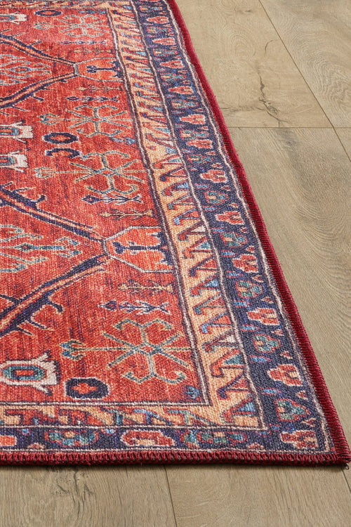 Load image 1 in gallery view. The image shows a corner of the Rhapsody Authentic Red Washable Rug - LCC3033, featuring blue and beige geometric designs on a light wood floor. Its detailed border and durable construction make it ideal for high-traffic spaces.