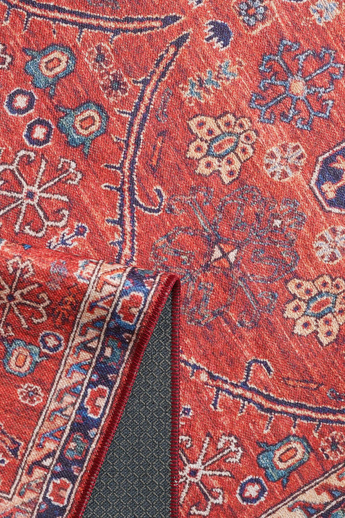 Load image 1 in gallery view. The Rhapsody Authentic Red Washable Rug - LCC3033 features intricate blue, cream, and gold floral and geometric designs. Its dark, diamond-patterned non-slip backing makes it ideal for high-traffic areas. One corner is shown folded over.