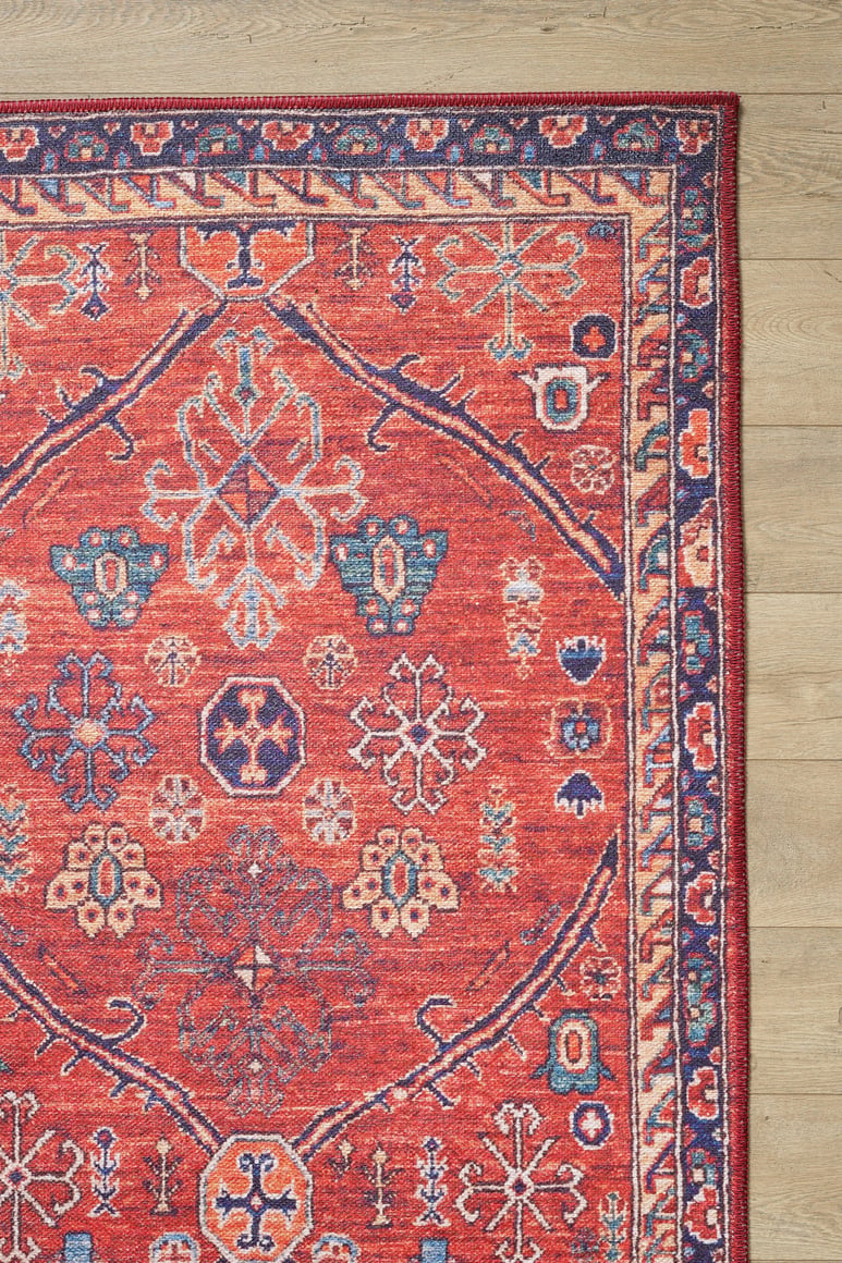 The Rhapsody Authentic Red Washable Rug - LCC3033 (Custom Size) features blue, cream, and orange geometric and floral designs with a motif border—perfect for high-traffic areas, shown here on a light wooden floor.