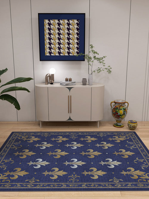 Load image 1 in gallery view. A modern room with a white cabinet, geometric art, potted plants, ceramics, and the Royal Fleur - Washable Rug - JRS016 featuring blue, gold, and white fleur-de-lis patterns—an allergy-sensitive choice for high-traffic areas.