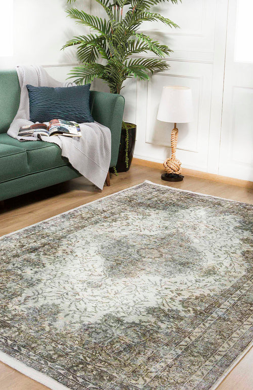 Load image 1 in gallery view. A living room with a green sofa, gray throw, open magazine, potted plant, rope-style floor lamp, and the Royal Legacy - Washable Rug - JR207 (Custom Size), ideal for high-traffic areas, on wooden floors and white paneled walls.