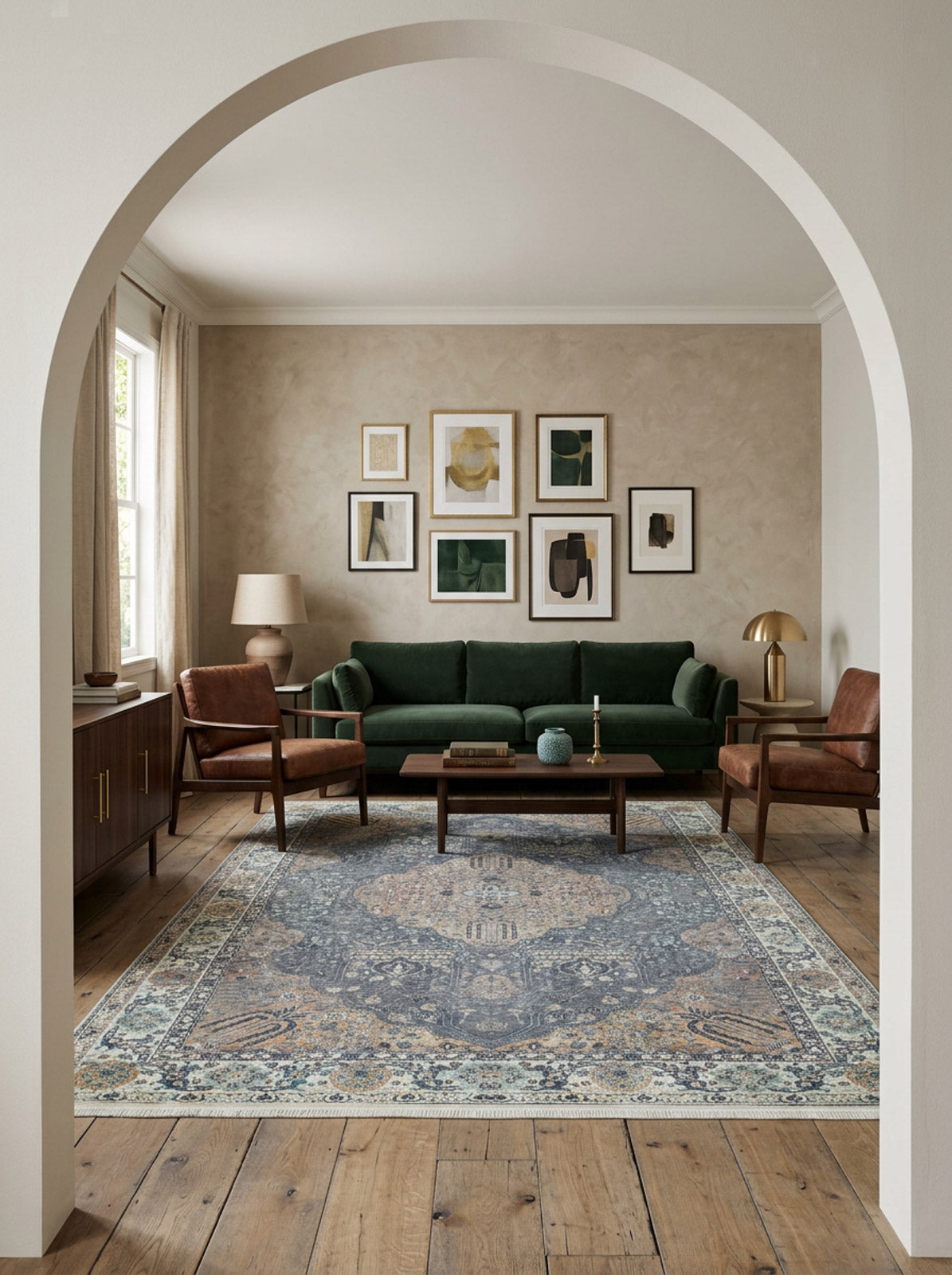 A stylish living room features a green sofa, two brown armchairs, wooden floor, modern art, a floor lamp, and the Royal Sultan - Washable Rug - JR1970 in blue for high-traffic areas, all framed by a white archway.