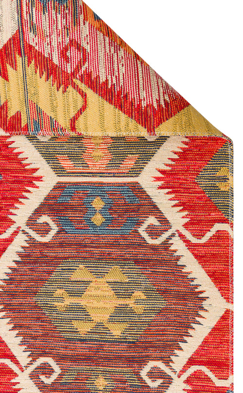 Load image 1 in gallery view. A close-up of the Ruby Grain - Kilim - NMD06 showcases its vibrant geometric tribal patterns in red, yellow, blue, and cream. The folded corner highlights the detailed flatwoven polyester design on both sides.