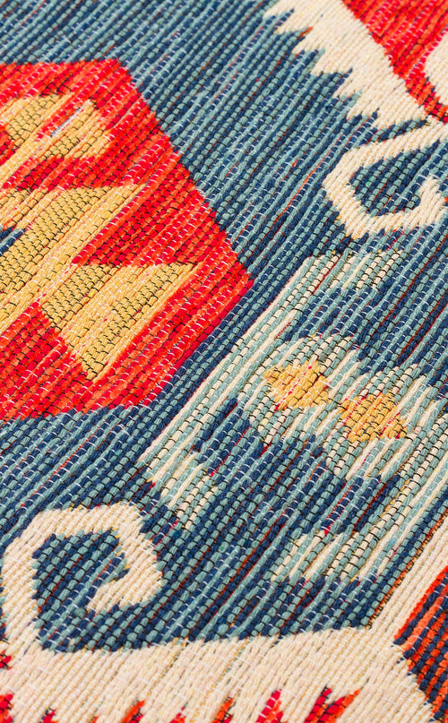 Load image 1 in gallery view. Close-up of Ruby Grain - Kilim - NMD06 featuring a geometric tribal pattern in red, blue, white, and yellow with zigzag and wave shapes and two small yellow stars on a blue background.