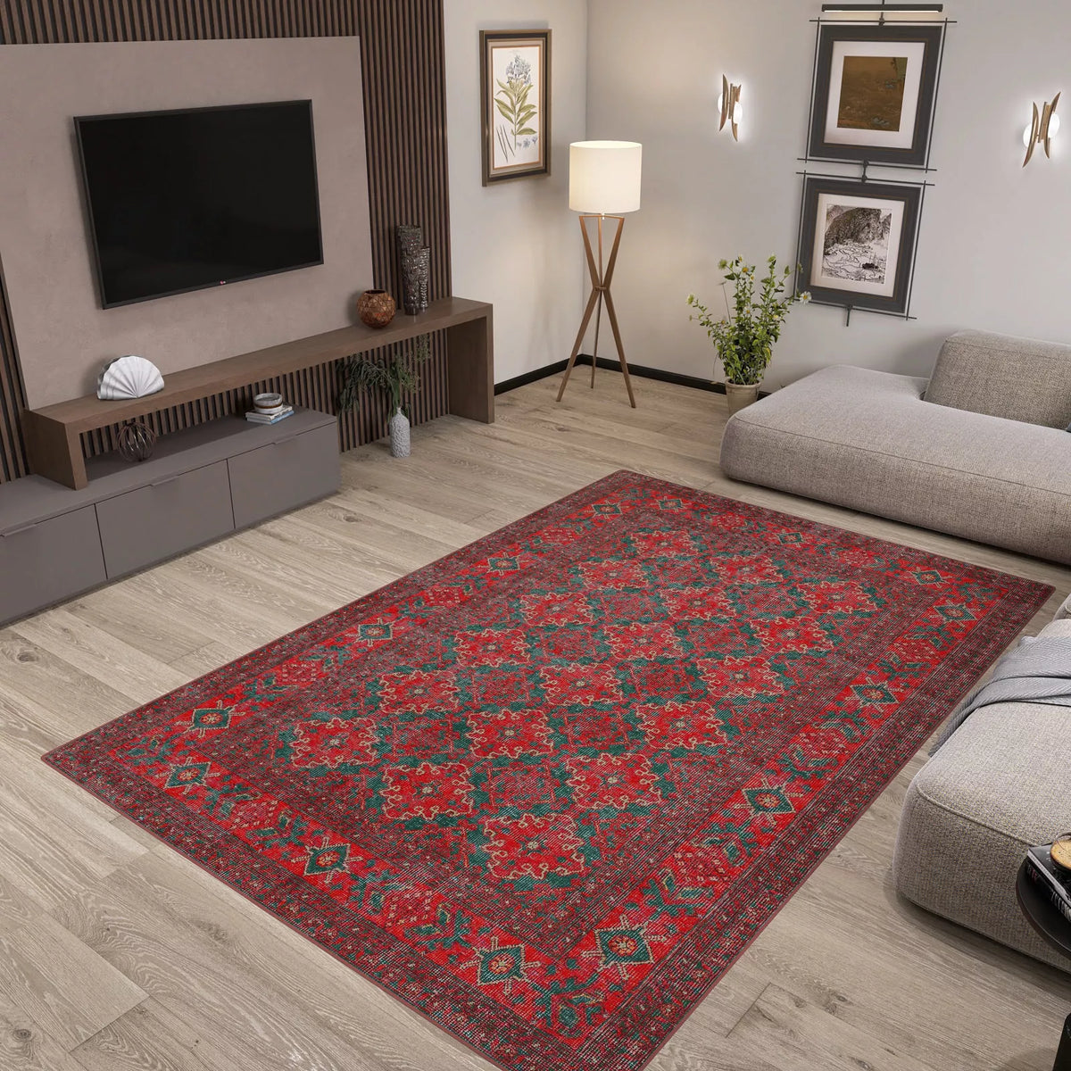 A modern living room with light wood floors, gray furniture, plants, wall art, and a Ruby Medallion - Washable Rug - JRN1031 (Custom Size) featuring a red pattern—ideal for high-traffic areas—centered in the space beneath a sleek media console and TV.