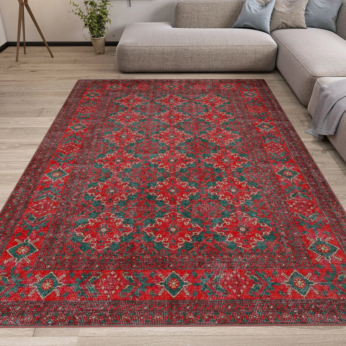 The Ruby Medallion - Washable Rug - JRN1031 (Custom Size) features red patterns with green and gold accents, shown on a light wood floor in a modern living room with a gray sectional, making it perfect for high-traffic or allergy-sensitive spaces.