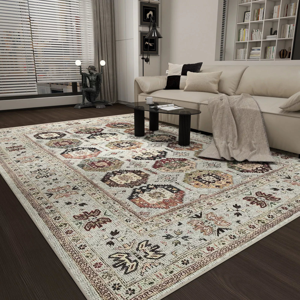 A modern living room with a beige sofa, glass coffee table, and the Rust Mosaic - Washable Rug - JRN1036, showcasing intricate geometric and floral designs in cream, brown, and red. Shelving and large windows complete the scene.
