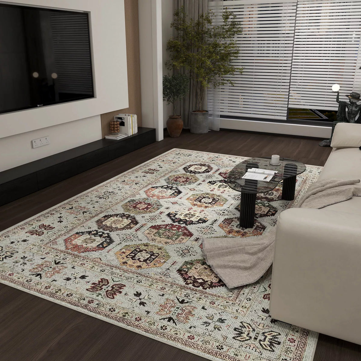 A modern living room with the Rust Mosaic - Washable Rug - JRN1036, a light-colored sofa with a throw, glass coffee table, wall-mounted TV, plant by the window, and floor-to-ceiling blinds letting in natural light.