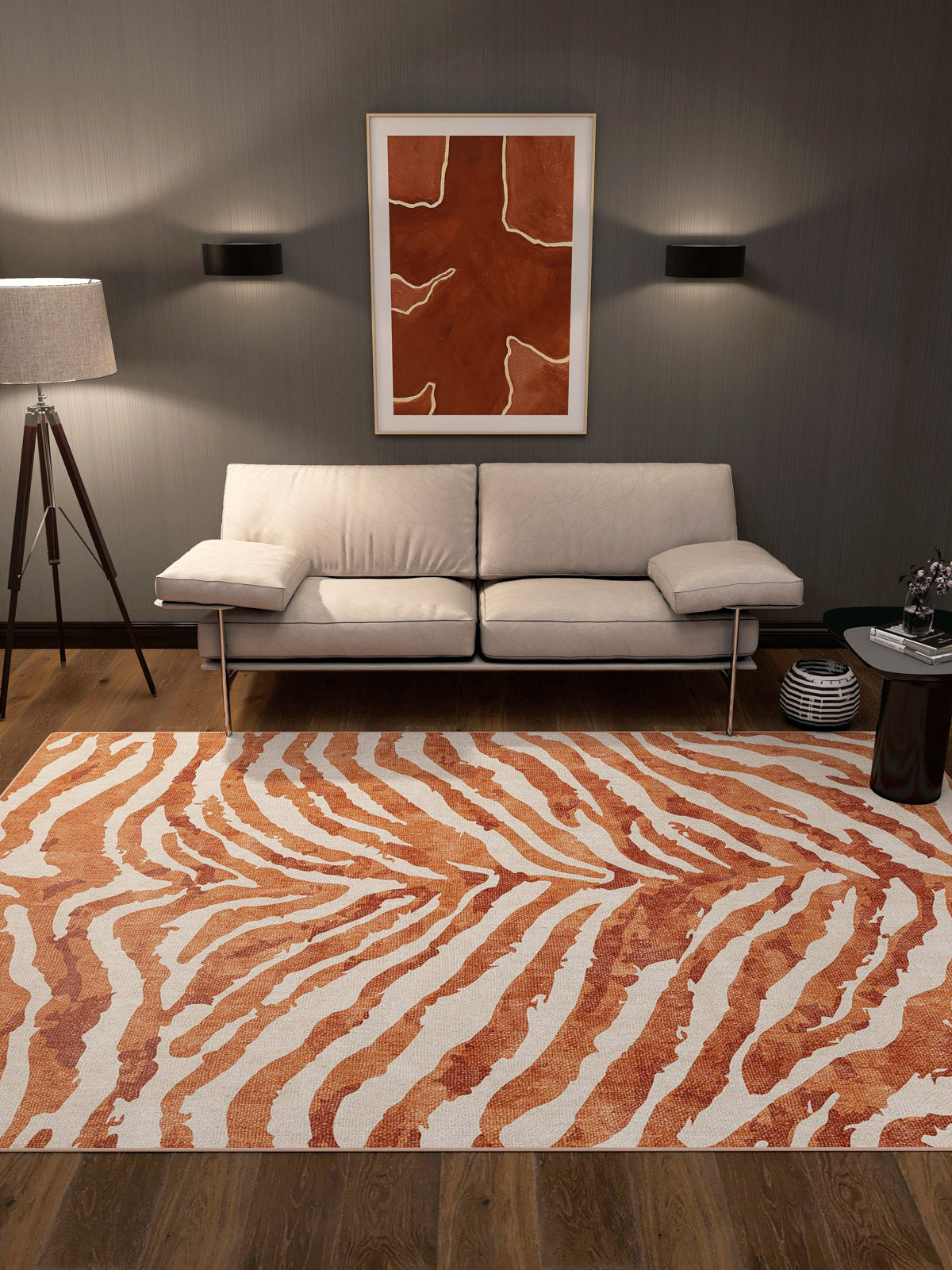 Contemporary living room with a cream sofa, floor lamp, round side table, and the Rustic Mirage - Washable Rug - JRN40 in orange and white zebra-like stripes—perfect for high-traffic areas. An abstract orange artwork hangs above the sofa on a dark gray wall.