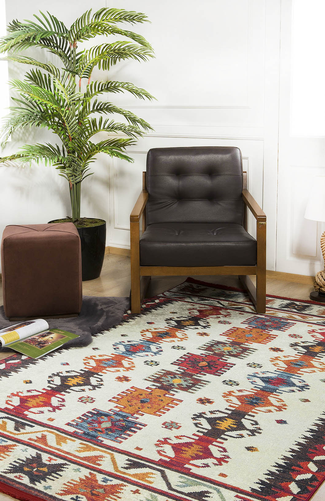 A brown armchair sits beside a potted plant and ottoman on the Rustic Refrain - Washable Rug - JR149 (Custom Size) in a bright room with white walls, with a rolled-up magazine on the floor.