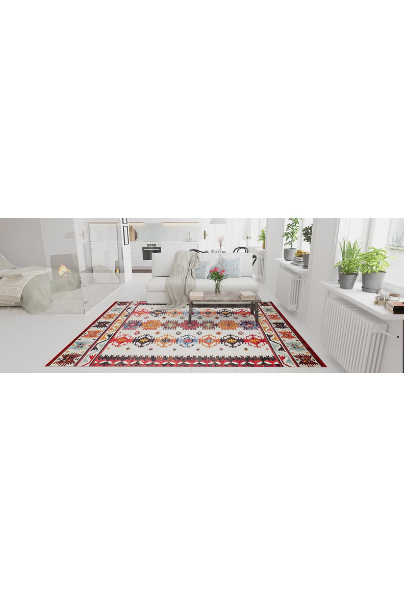 A bright living room with white walls and furniture, featuring the Rustic Refrain - Washable Rug - JR149 (Custom Size), a cushioned bench with a throw, potted plants on window sills, and a fireplace in the background.