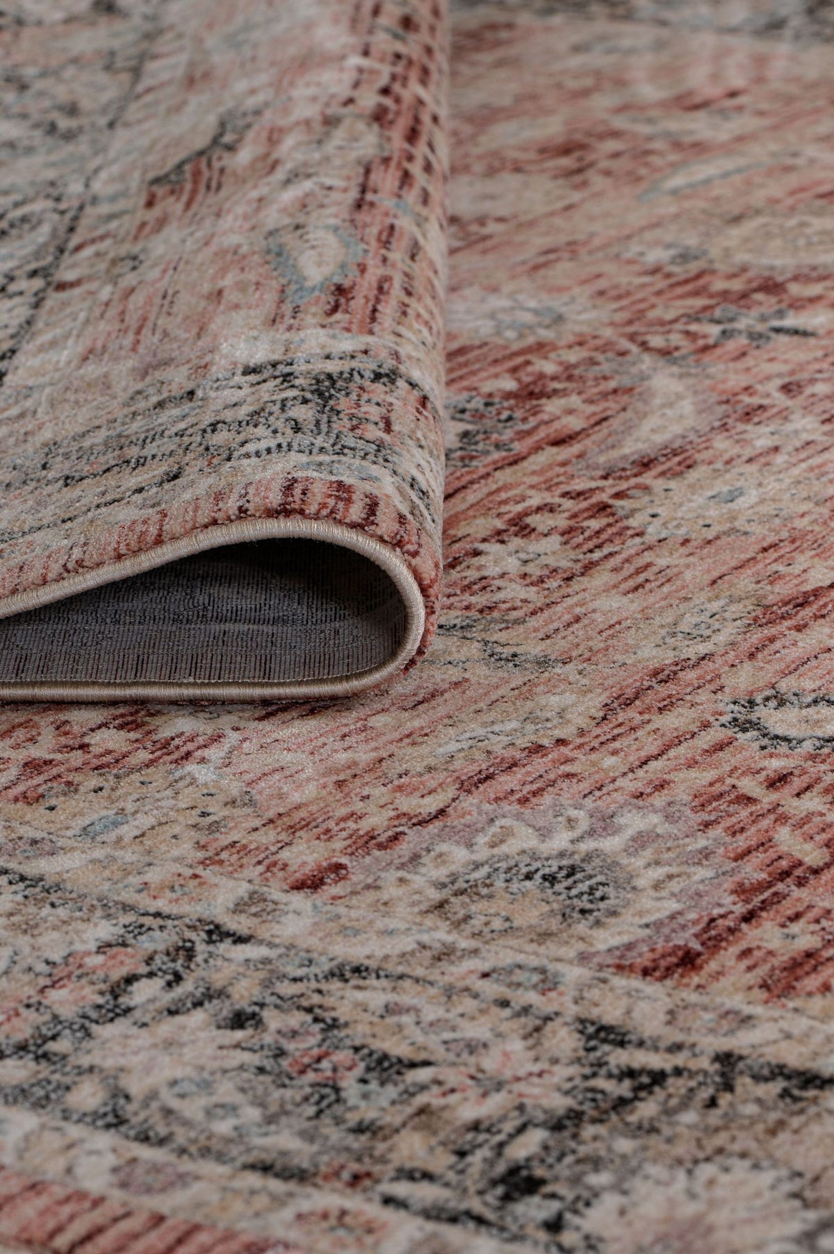 A close-up of the Rustic Bloom - Area Rug - APX2961 in red and beige muted tones, featuring a subtle floral motif and one corner folded to show the texture and underside of this Persian vintage-inspired area rug.