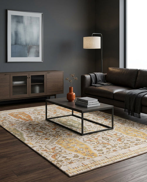 Load image 1 in gallery view. A modern living room featuring a dark leather sofa, floor lamp, wooden cabinet, minimalist coffee table, and the Saffron Heritage Area Rug APX1912 with yellow and orange motifs, complemented by abstract art on a dark gray wall.