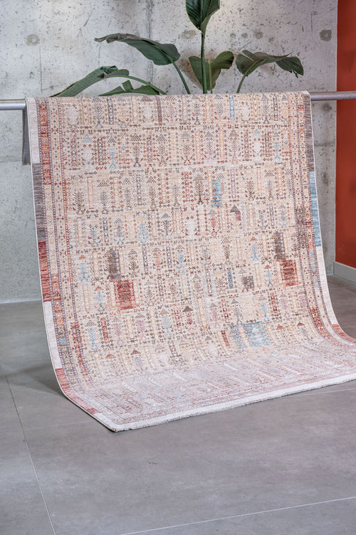 Load image 1 in gallery view. Beige rug with a multi-colored abstract geometric and tree-like pattern, draped over a rack in a studio setting.