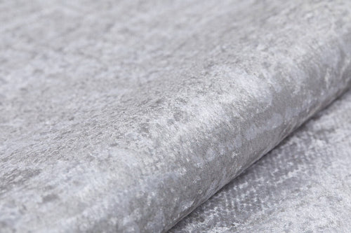 Bild 1 in Galerieansicht laden. Close-up of the Sea Spray - Washable Rug - JR847 (Custom Size) in light grey velvet with a soft, subtly shiny texture and irregular patterns. Plush material, reminiscent of cream and beige rugs, is folded to highlight its smooth surface.