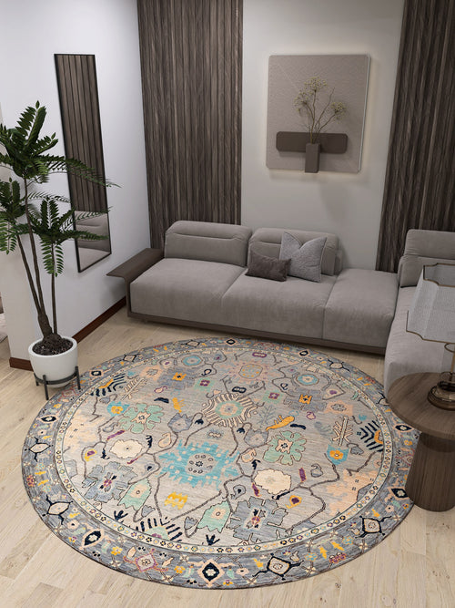 Load image 1 in gallery view. A modern living room with a gray sectional, Seraphix Pastel Bordered Washable Rug - LCC3011 for high-traffic areas, pastel hues, a potted plant, wooden accents, wall décor, and a small round side table on light wood flooring.