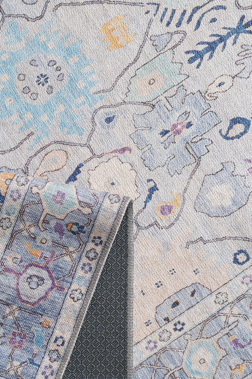 Load image 1 in gallery view. A close-up of the Seraphix Pastel Bordered Washable Rug (LCC3011) in blue, cream, and pastel hues with floral and geometric patterns; a folded corner shows its dark non-slip backing—perfect for high-traffic areas.