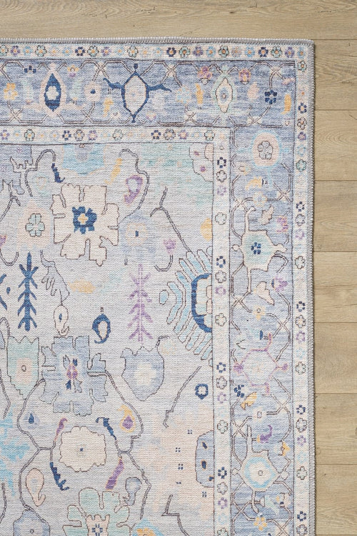 Load image 1 in gallery view. The Seraphix Pastel Bordered Washable Rug - LCC3011 features soft blue, lavender, and cream tones with floral and geometric designs plus a decorative border, shown on a light wood floor—ideal for high-traffic areas.