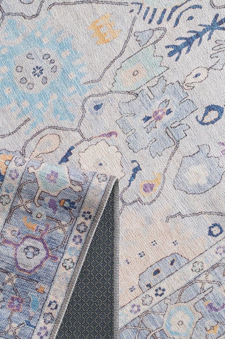 A close-up of the Seraphix Pastel Bordered Washable Rug - LCC3011 (Custom Size) shows its blue, beige, and yellow geometric and floral design with a folded corner revealing dark backing—perfect for high-traffic areas.