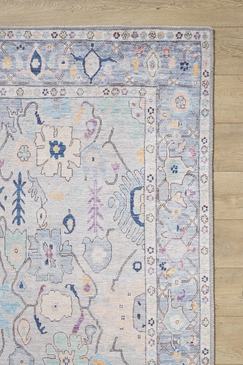 The image shows the Seraphix Pastel Bordered Washable Rug - LCC3011 (Custom Size), featuring blue, cream, and lavender floral and geometric motifs, ideal for high-traffic areas, placed on a light wood floor.