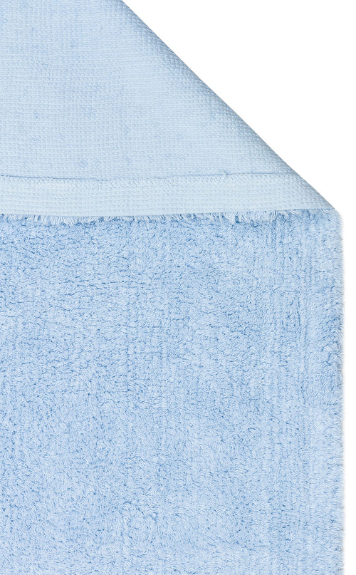 Load image 1 in gallery view. A close-up of the Sky Nap - Washable Shaggy - CBNPLAIN towel in light blue, highlighting its plush, textured fabric and tidy stitched edge, with a folded corner revealing both sides of the soft material.