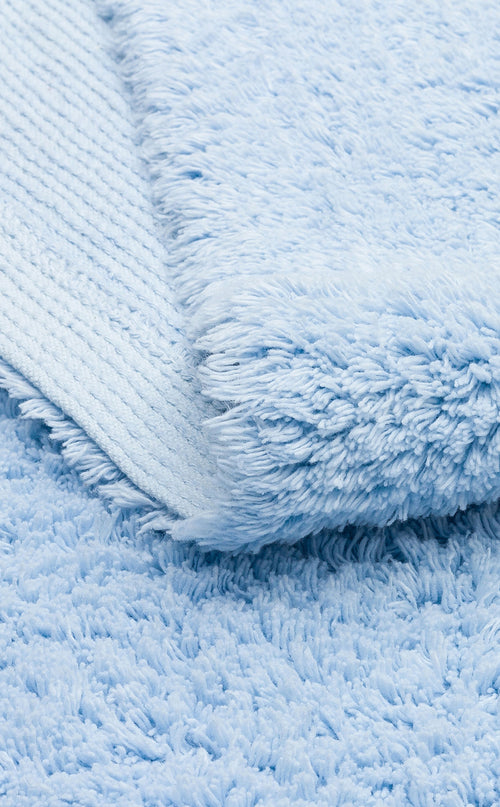 Load image 1 in gallery view. A close-up of the Sky Nap - Washable Shaggy - CBNPLAIN rug displays its soft blue, plush cotton texture and cozy thickness, with a neatly folded corner highlighting its shaggy surface.