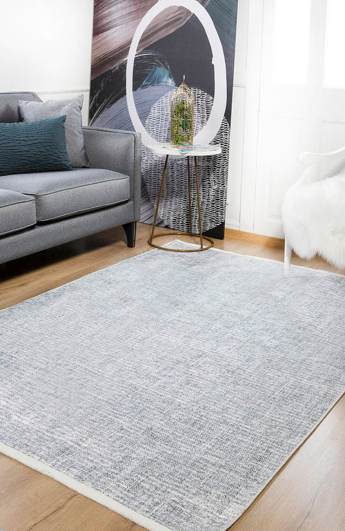 Load image 1 in gallery view. A modern living room featuring a gray sofa, the Softly Chic - Washable Rug - JR747 in light gray, a white fur chair, a round side table with a decorative birdcage, and abstract art propped near a bright window.