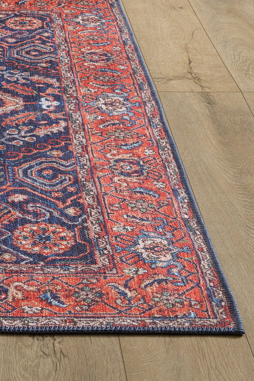 Bild 1 in Galerieansicht laden. A close-up of the Solstice Red Navy Washable Rug - LCC3026 with geometric and floral motifs, shown on a light wood floor. Only part of this allergy-sensitive rug and flooring is visible.
