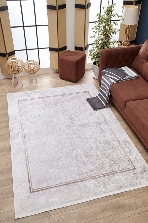 Load image 1 in gallery view. A living room with the Sophisticated Edging - Washable Rug - JR1738 (Custom Size) on wood floors, a brown sofa, striped throw, ottoman, plant, and wicker tables by large windows—perfect for allergy-sensitive homes.