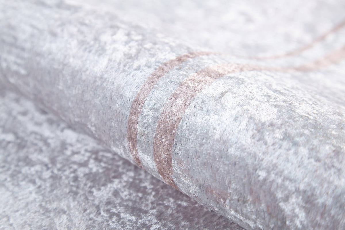 A close-up of the Sophisticated Edging - Washable Rug - JR1738 (Custom Size) shows silvery-gray textured fabric with a subtle sheen and faint curved taupe lines, offering a soft, allergy-friendly, washable, and easy-to-maintain material.