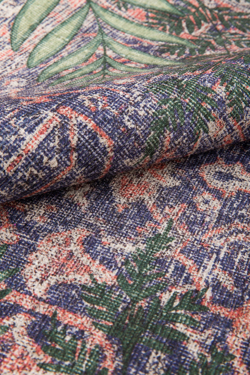 Bild 1 in Galerieansicht laden. A close-up of the Stormstripe Echo - Washable Rug (JR0046), showing its thick, woven texture and multicolored pattern with green leaves and abstract shapes in blue, red, and cream. The fabric is slightly folded to highlight the weave detail.