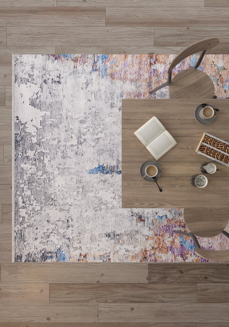 A modern dining scene from above with a wooden table, two chairs, coffee cups, a book, and breadsticks atop the Striking Statements - Washable Rug - JR786, a vibrant multicolor flat weave that’s stylish and practical on wooden flooring.