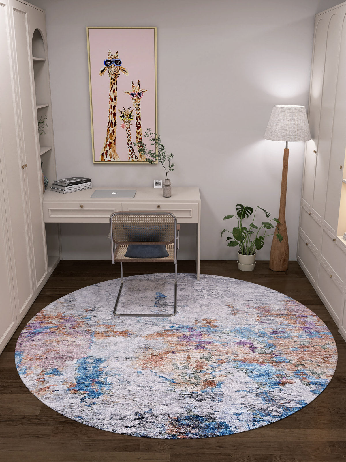 A home office with a white desk, laptop, rattan chair, Striking Statements - Washable Rug - JR786 (Custom Size), standing lamp, potted plants, and a framed giraffe illustration on the wall.
